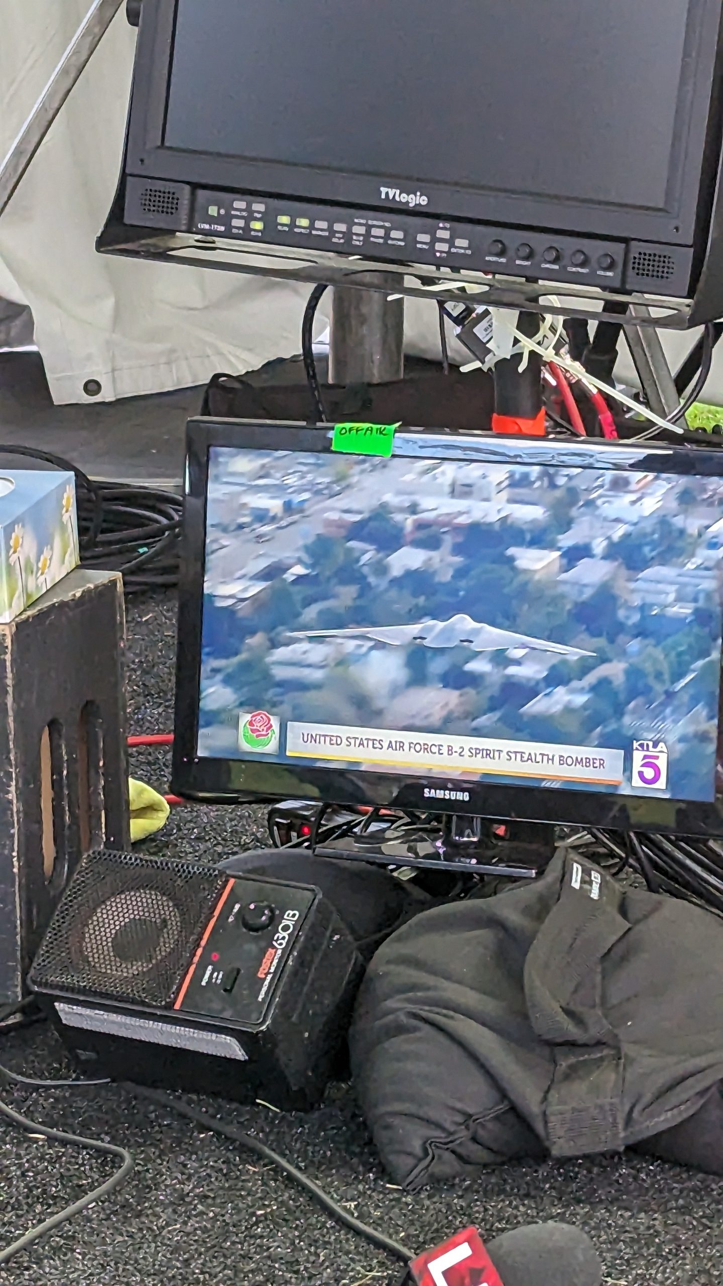 KTLA 5 broadcast monitor displaying a U.S. Air Force B-2 Spirit stealth bomber during Rose Parade coverage, surrounded by production equipment, cables and additional monitors.