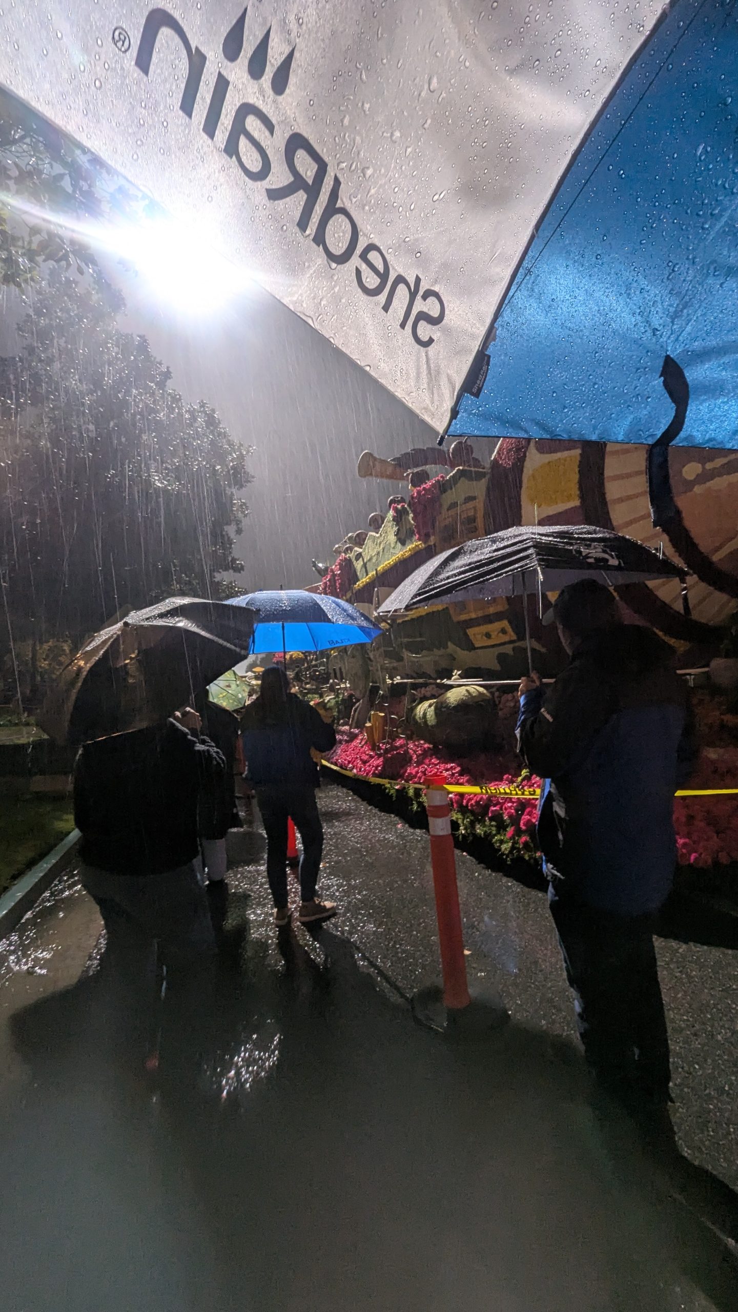 KTLA production crew walking along the wet Rose Parade route in Pasadena, before dawn, during rainy conditions in 2026.